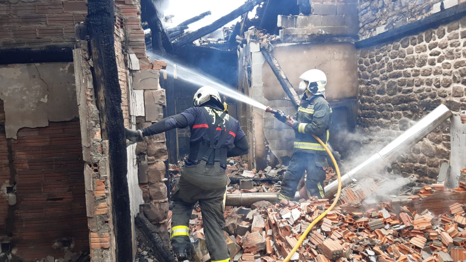 dos bomberos refrescando el escombro generado